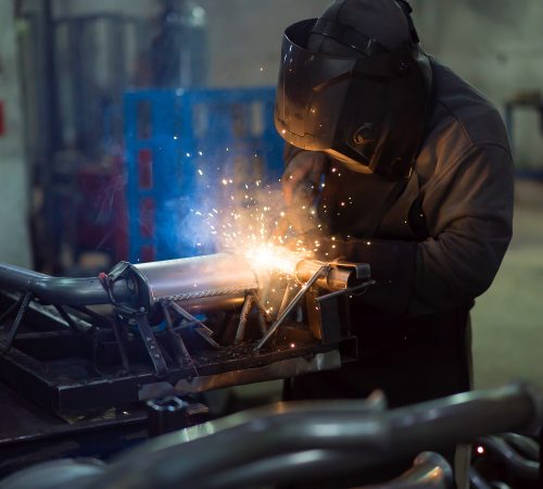 worker welding exhaust pipes pieces together